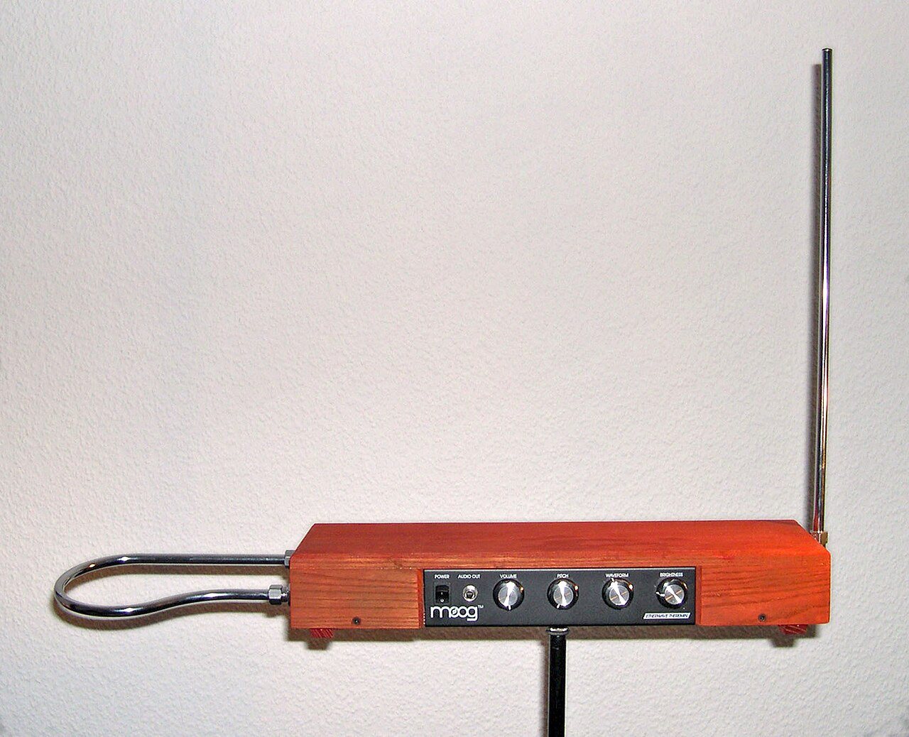 A Moog Etherwave theremin in a wooden case on a stand, with a straight pitch antenna on the right and a looped volume antenna on the left